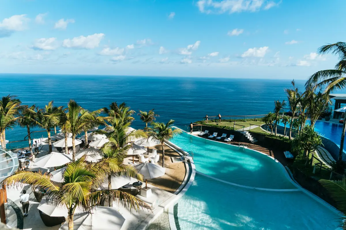An infinity pool lined with palms, the sea beyond
